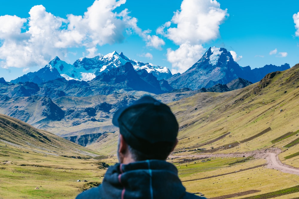 man in green hoodie standing near brown mountain under white clouds and blue sky during daytime