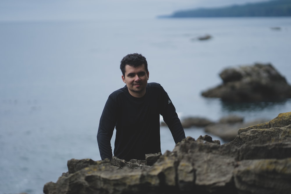 man in black long sleeve shirt sitting on rock near body of water during daytime