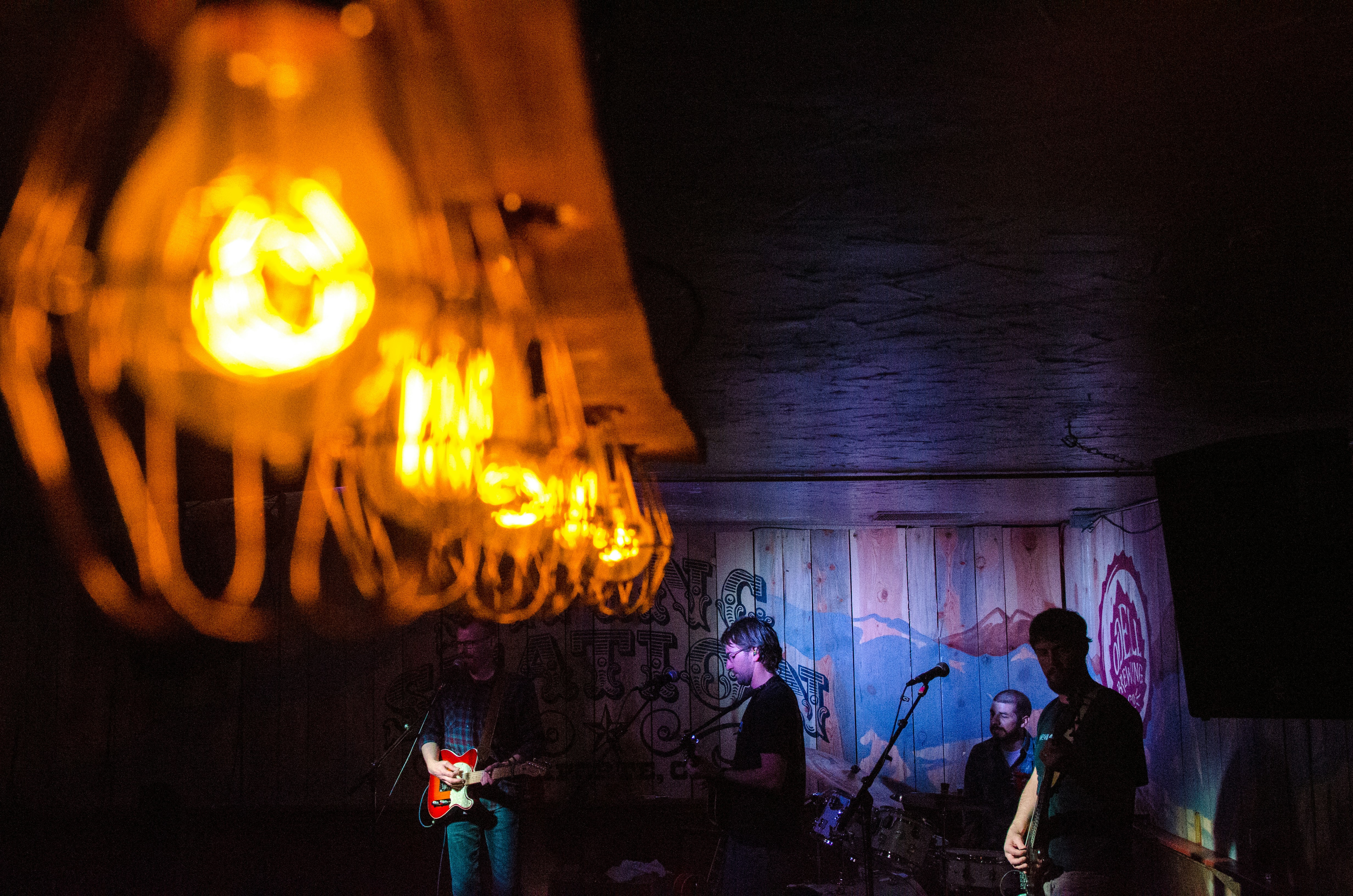 A four piece band performs on a rustic stage.