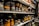 Shelves filled with rows of various pairs of boots and shoes are seen, each with labels and tags attached for identification. The footwear appears to be organized meticulously, possibly indicating a storage area or inventory space. The room lighting creates a warm tone, highlighting the textures and materials of the shoes.