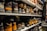 Shelves filled with rows of various pairs of boots and shoes are seen, each with labels and tags attached for identification. The footwear appears to be organized meticulously, possibly indicating a storage area or inventory space. The room lighting creates a warm tone, highlighting the textures and materials of the shoes.