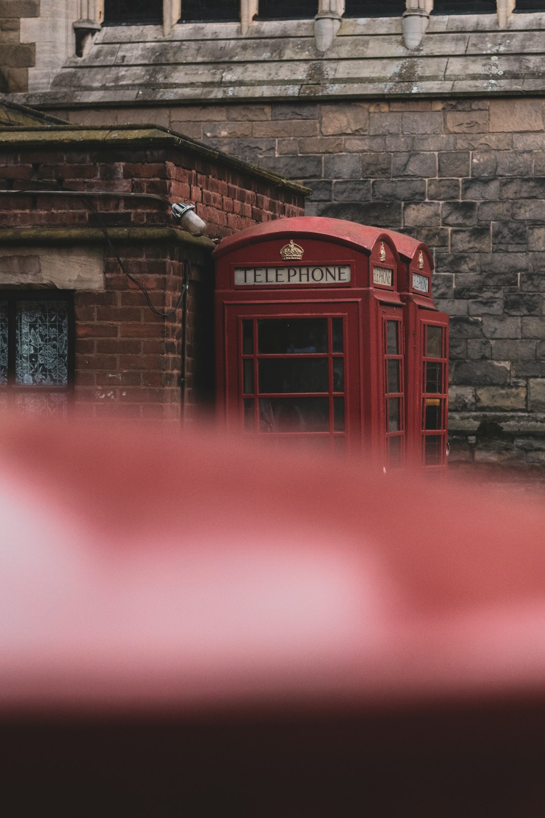 red telephone booth beside brown brick wall