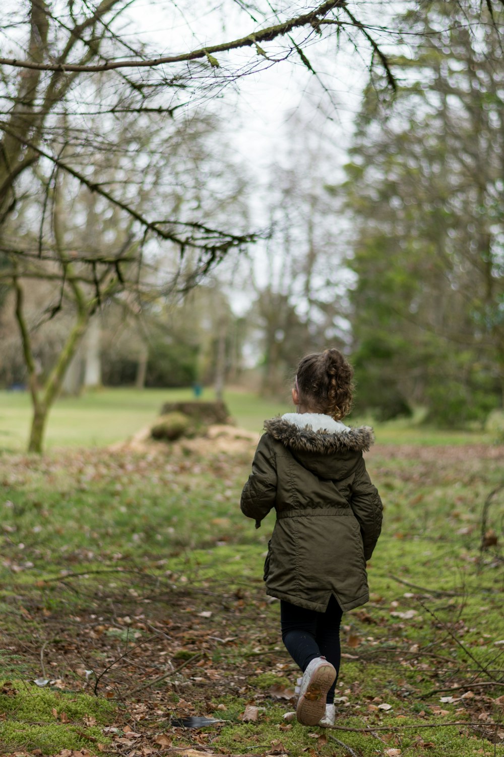 child in green jacket walking on green grass field during daytime