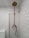 A bathroom with white subway tiles covering the walls, a vintage-style brass shower fixture that includes a showerhead at the top and a faucet below, and a modern toilet partially visible to the left. The overall look is clean and minimalistic.