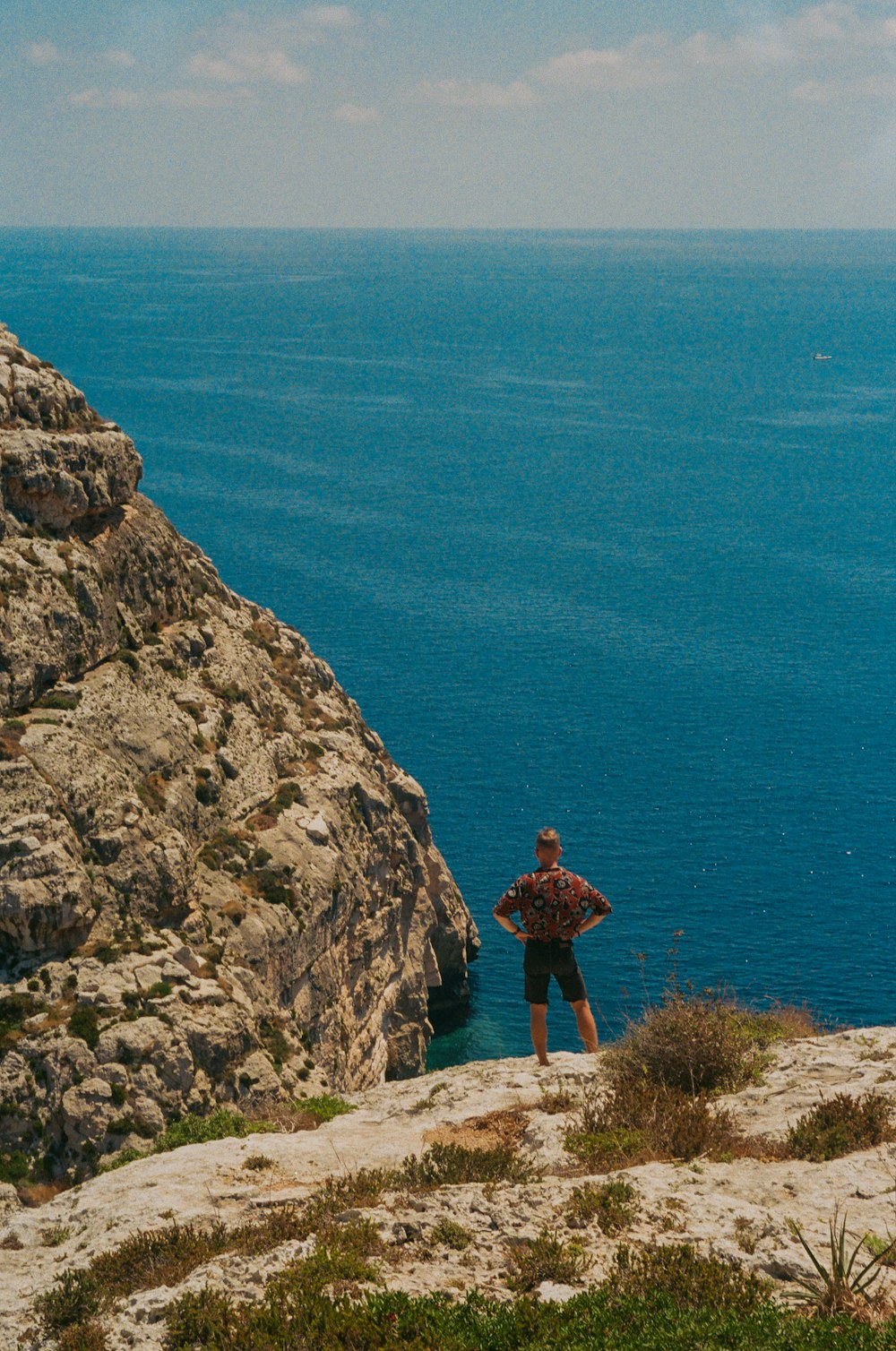 昼間、青い海の近くの岩層に立つ茶色のドレスを着た女性