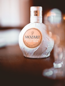 A bottle of Mozart White Chocolate Vanilla Cream liqueur sits on a wooden surface with its decorative packaging. The background is softly blurred, adding elegance to the presentation.