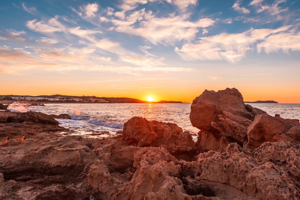 brown rock formation near body of water during sunset