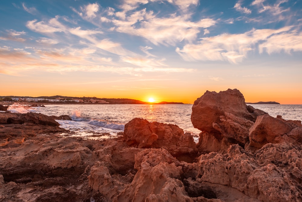 Formación de roca marrón cerca del cuerpo de agua durante la puesta del sol