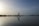 A person is practicing yoga in a warrior pose on the beach, reflected on the calm water. The sky is vast with a blend of light and darker shades, creating a serene and peaceful atmosphere. The horizon is lined with distant trees and a gentle hill on the right.