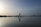 A person is practicing yoga in a warrior pose on the beach, reflected on the calm water. The sky is vast with a blend of light and darker shades, creating a serene and peaceful atmosphere. The horizon is lined with distant trees and a gentle hill on the right.