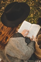 woman in gray sweater and black hat reading book