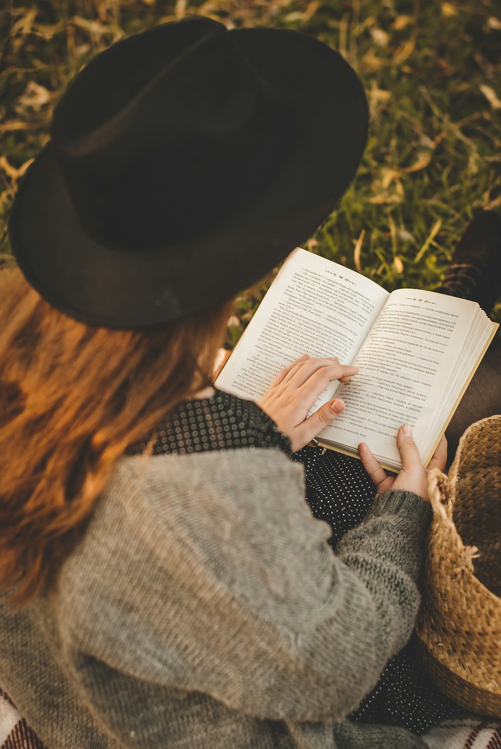 woman in gray sweater and black hat reading book