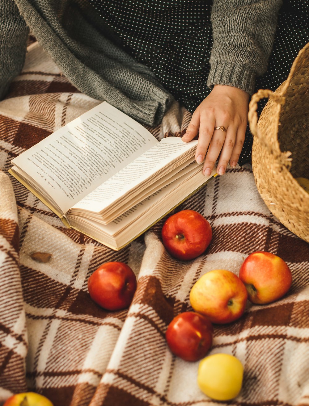 person holding book page with red apple fruits on brown woven basket