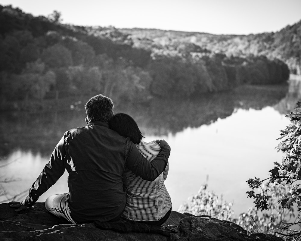 man in black and white striped long sleeve shirt sitting on rock near lake