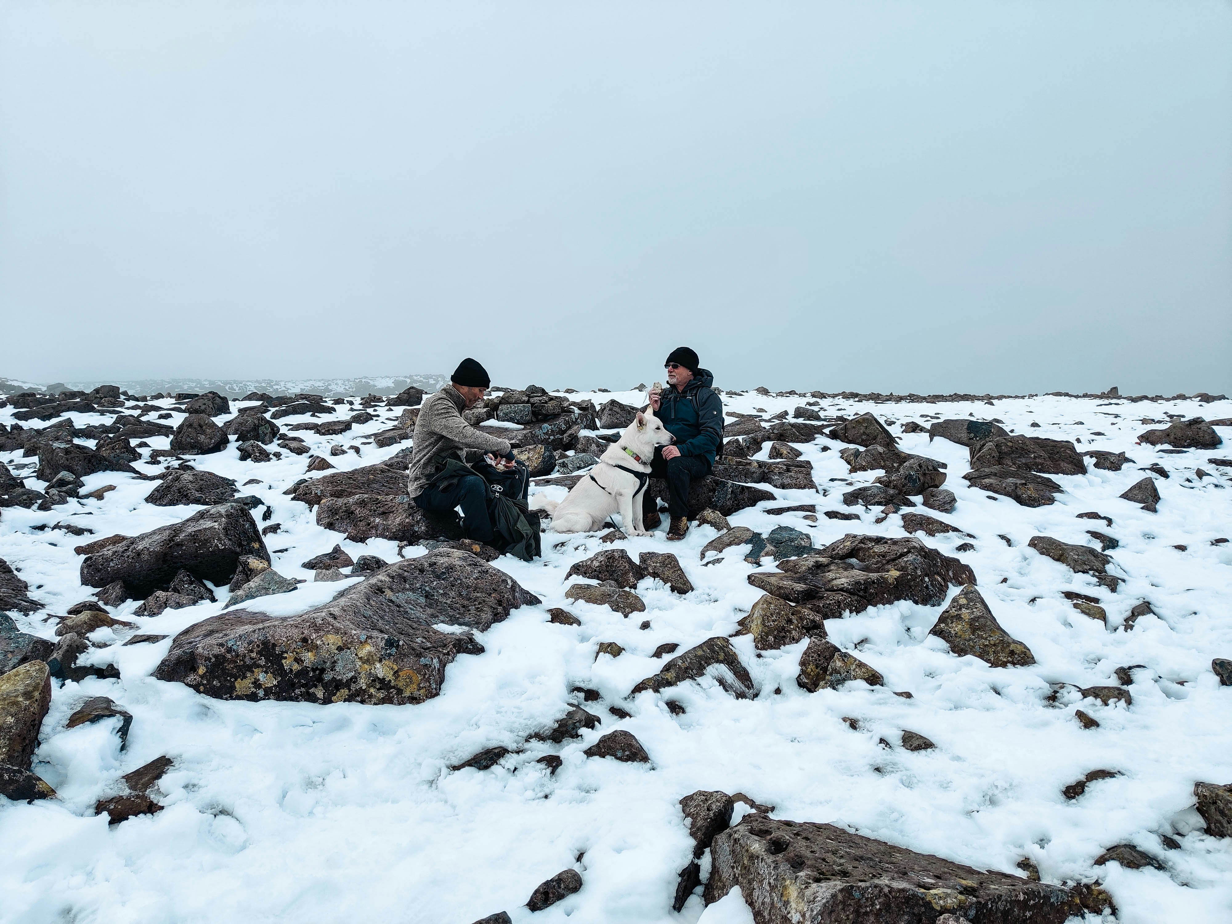 people sitting on rock formation covered with snow during daytime