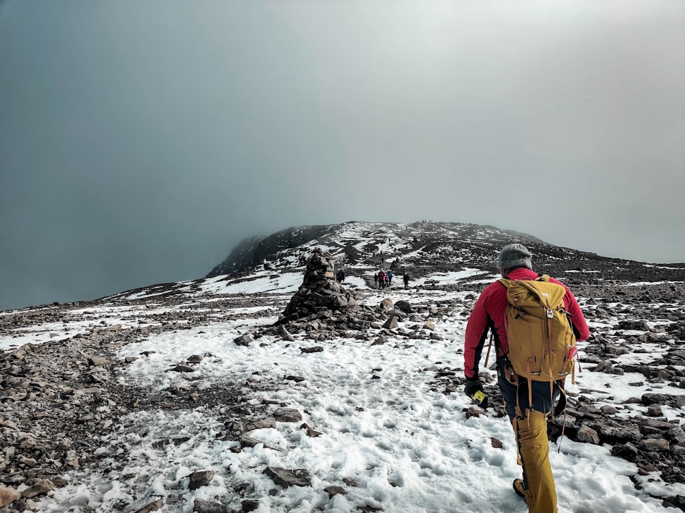 man in yellow jacket and brown pants walking on snow covered ground during daytime