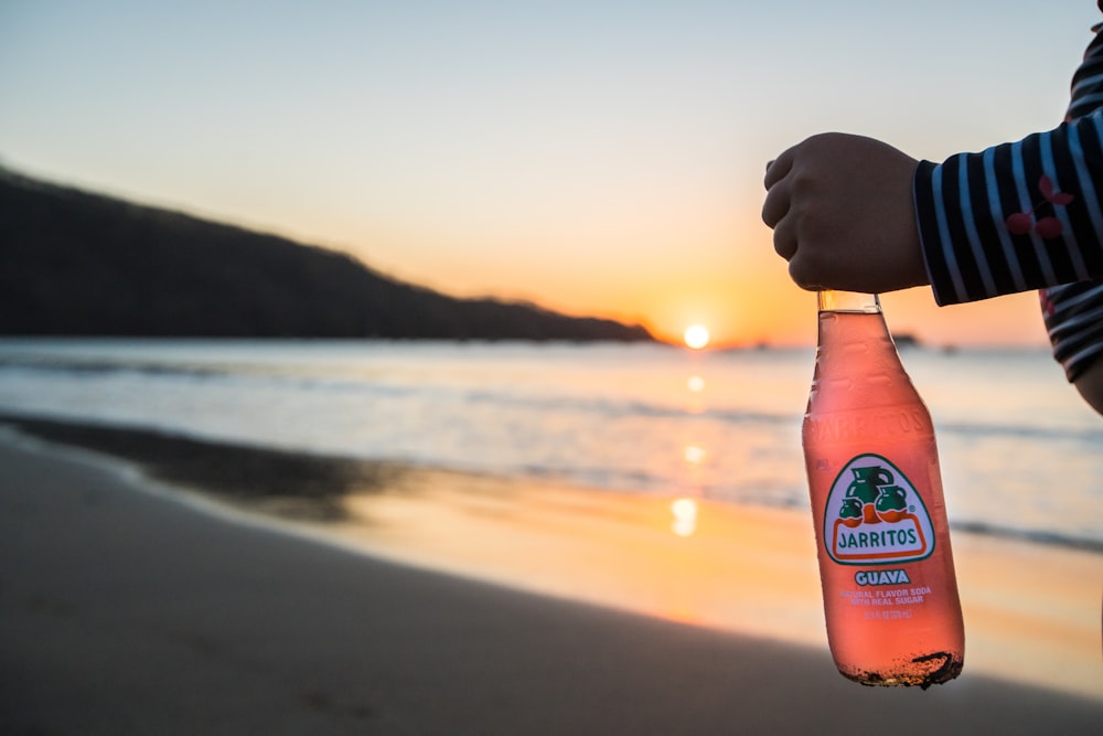 person holding blue and white bottle during sunset