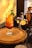 A refreshing cocktail sits on a wooden board, garnished with mint leaves and a lemon slice. Surrounding the drink are cocktail-making tools, including a jigger, shaker, and cut lemon slices. Warm lighting creates a cozy ambiance.