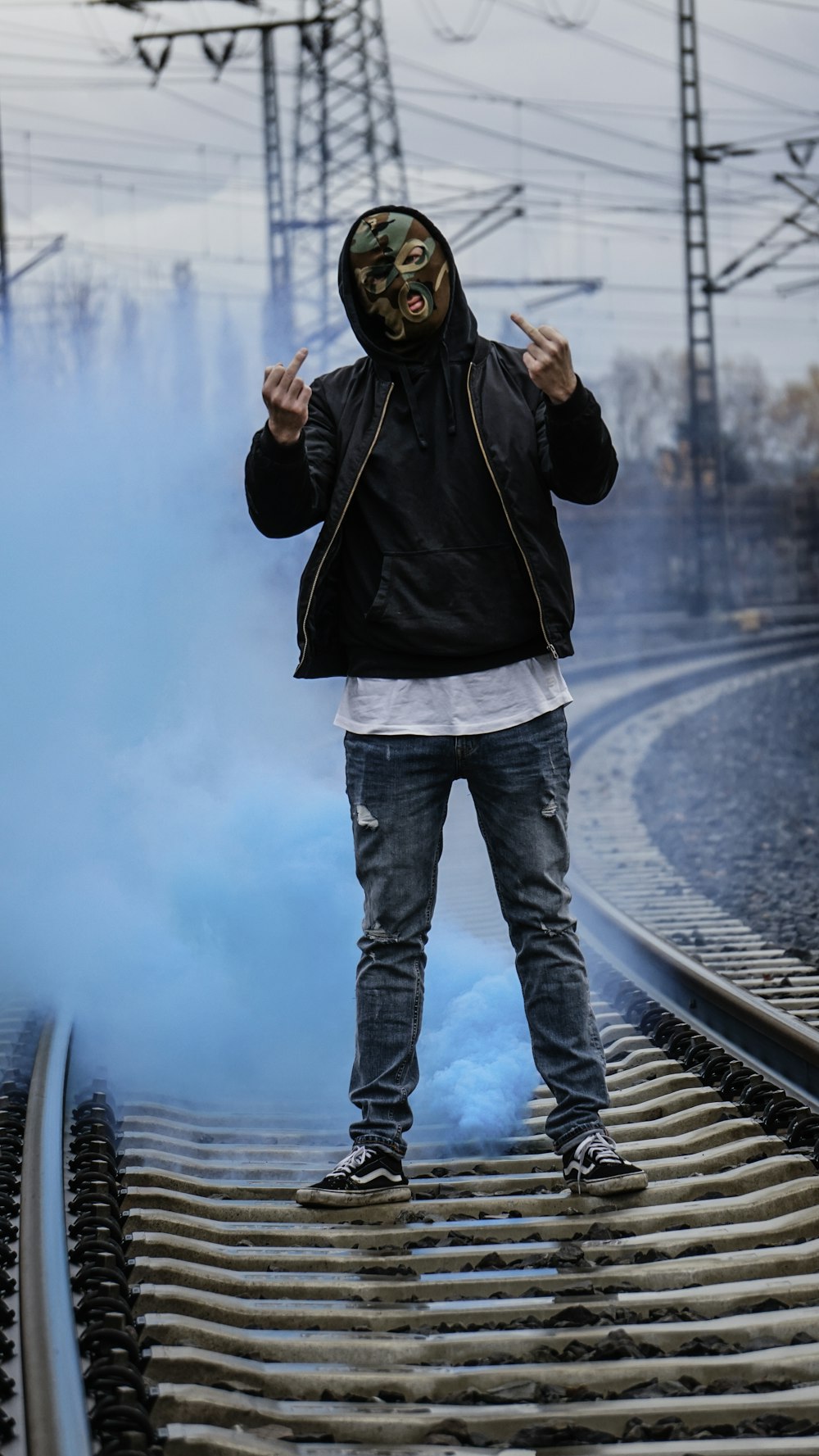 Hombre con chaqueta negra y jeans de mezclilla azul de pie en el riel del tren