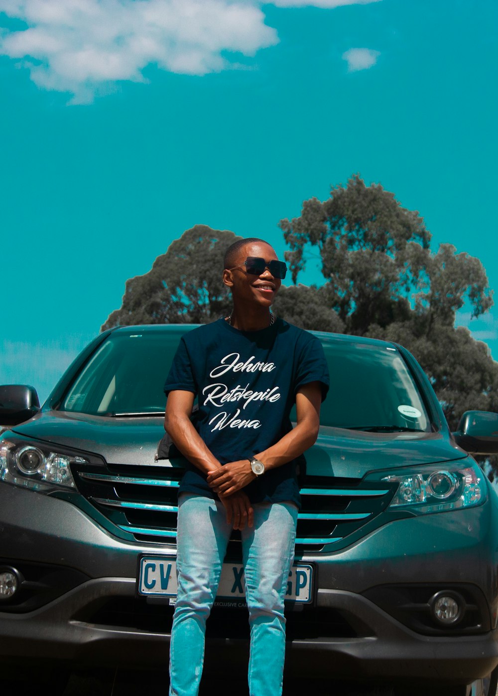 man in black crew neck t-shirt and gray denim jeans sitting on green car