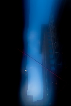 A cityscape with tall buildings on either side framing a bright blue sky. The edges of the photograph are dark, creating a vignette effect, and a diagonal red line cuts across the scene. The atmosphere appears to be serene yet slightly mysterious.