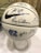 A white basketball decorated with numerous signatures and a large Nike logo. It features the logo and letters of the University of North Carolina, dated 2017-18. The ball is placed on a clear stand and is set against a neutral background.
