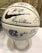 A white basketball decorated with numerous signatures and a large Nike logo. It features the logo and letters of the University of North Carolina, dated 2017-18. The ball is placed on a clear stand and is set against a neutral background.