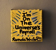 A small yellow canvas displays bold black text that reads 'I'm on the Universe's Payroll' with the artist's signature and date at the bottom. There are blue and gray radial lines emanating from the text, creating a dynamic visual effect.