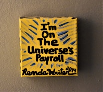 A small yellow canvas displays bold black text that reads 'I'm on the Universe's Payroll' with the artist's signature and date at the bottom. There are blue and gray radial lines emanating from the text, creating a dynamic visual effect.