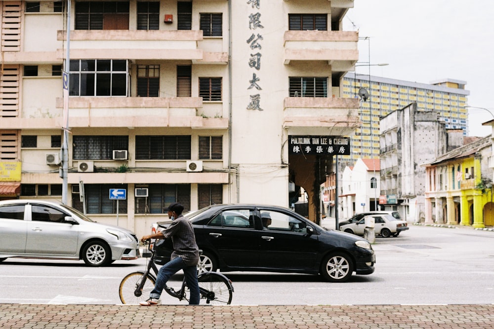 man in black jacket riding bicycle near black sedan during daytime