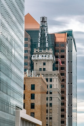 Several tall buildings are closely spaced together in an urban setting. The central building features a prominent sign with the words 'Walker Center.' Architectural styles range from modern glass facades to vintage brick and stone designs. An American flag is visible, adding to the cityscape.