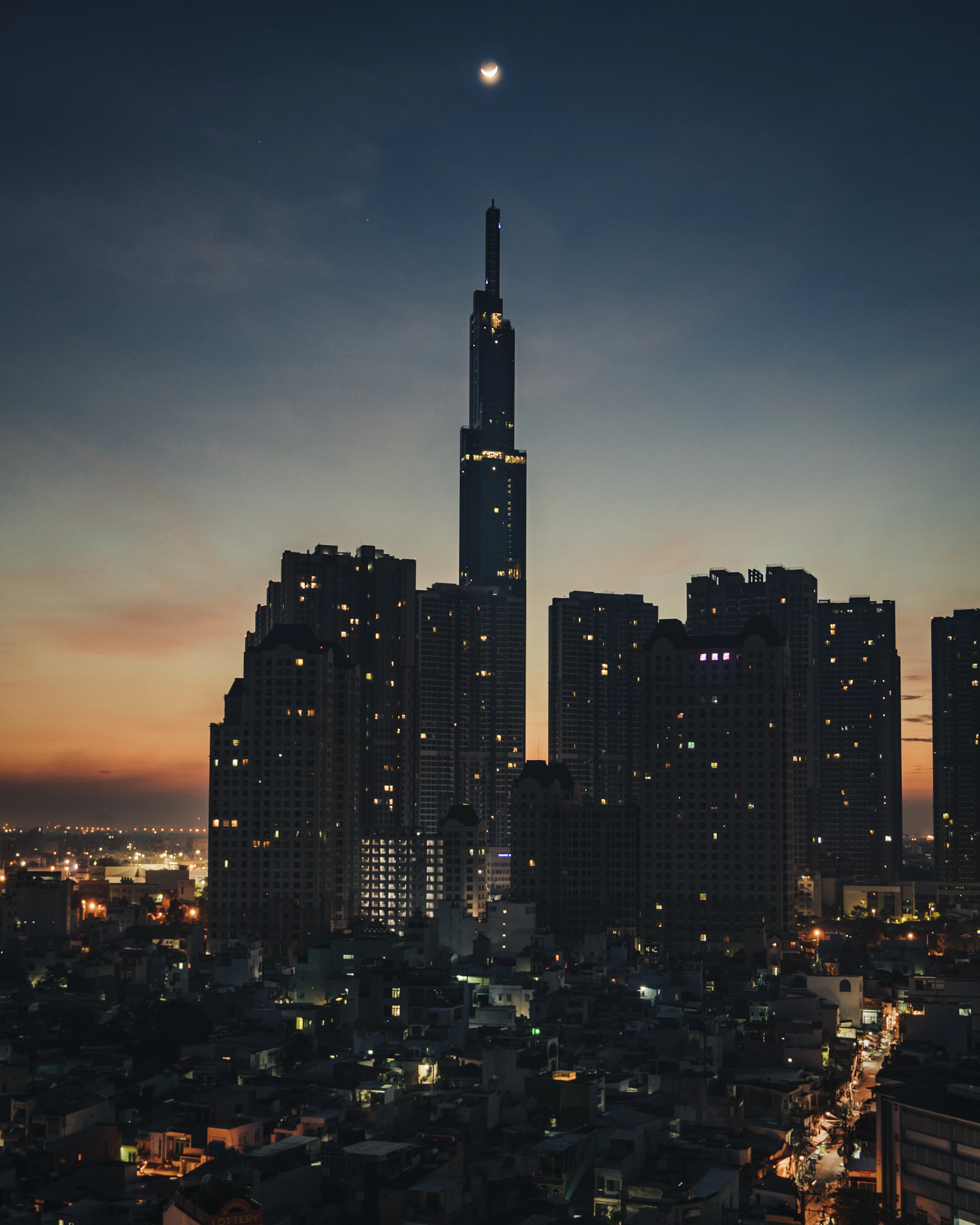 Landmark 81 skyscraper glows at dusk above the Ho Chi Minh City skyline under a crescent moon.