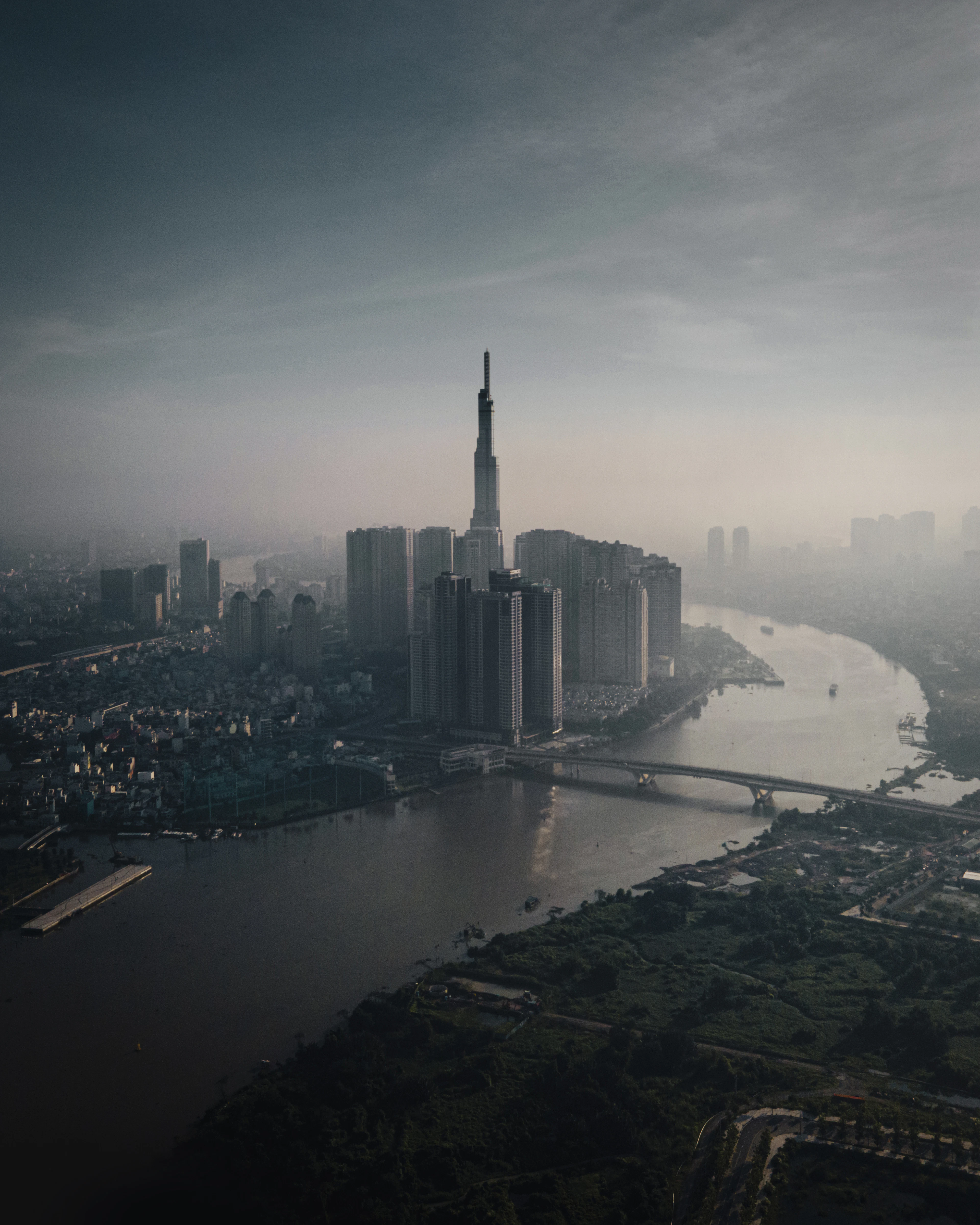Aerial dusk view of the Landmark 81 tower rising above the Saigon River in hazy light.