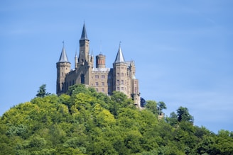 A majestic medieval castle surrounded by lush green hills under a bright blue sky.
