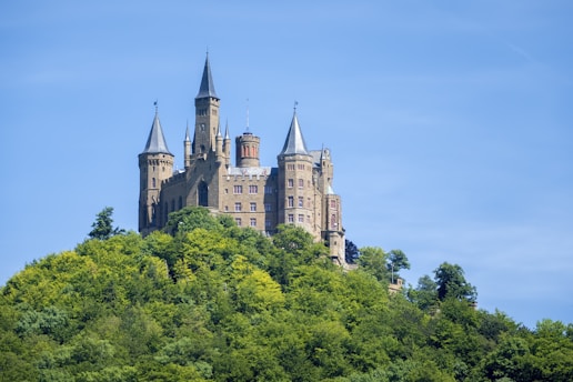 A majestic medieval castle surrounded by lush green hills under a bright blue sky.