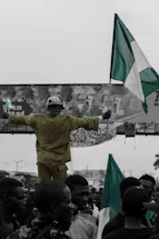 A diverse group of Nigerians smiling and holding flags at an international city landmark.