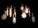 Several light bulbs with different shapes and filament designs hang against a dark background. The bulbs emit a warm glow, creating an inviting and intimate atmosphere.