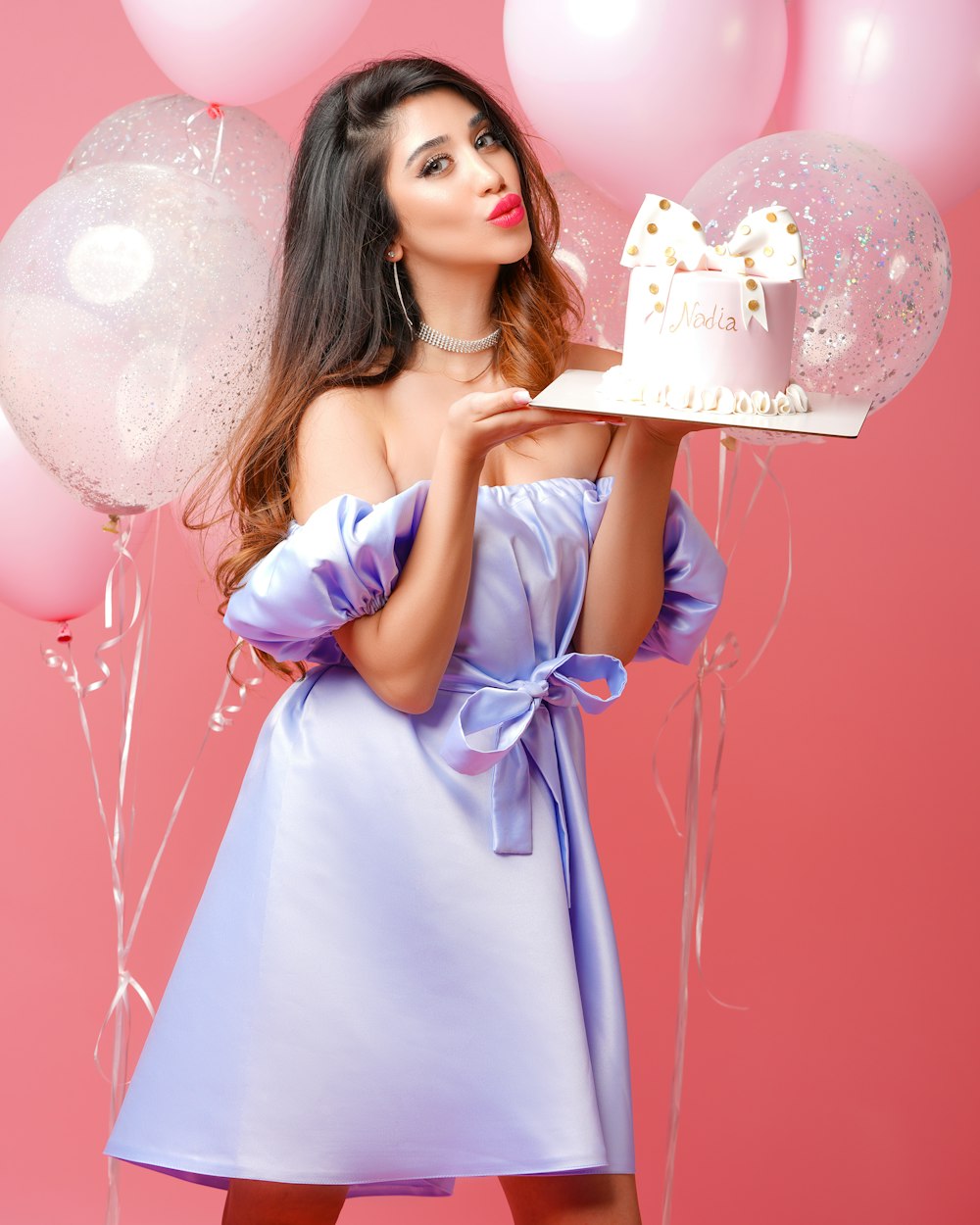 흰색과 분홍색 생일 축하 케이크를 들고 분홍색 드레스를 입은 여자