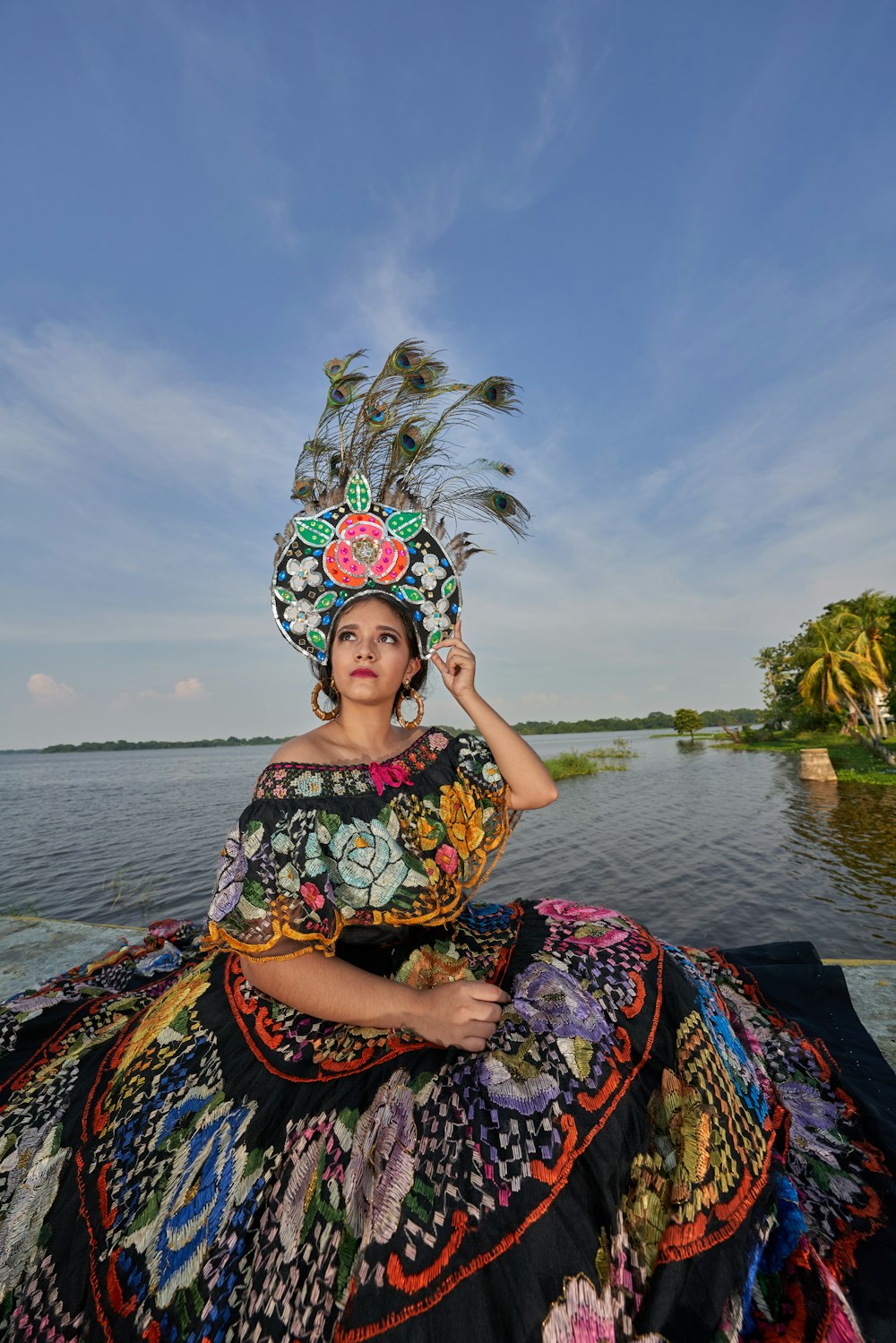 woman in blue and yellow floral dress wearing white floral headdress sitting on brown wooden dock