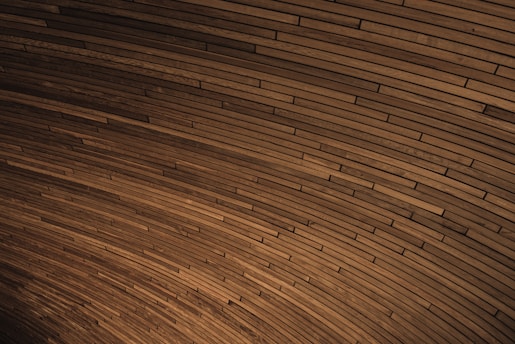 A curved pattern of wooden planks tightly arranged to create a visually engaging texture. The planks vary slightly in shade, contributing to a dynamic yet harmonious visual effect.
