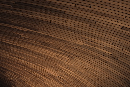 A curved pattern of wooden planks tightly arranged to create a visually engaging texture. The planks vary slightly in shade, contributing to a dynamic yet harmonious visual effect.