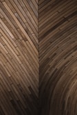 An intricate wooden pattern featuring a geometric design with overlapping planks creating a series of angled and curved sections. The wood is of a deep brown color, showcasing its natural grain and texture.