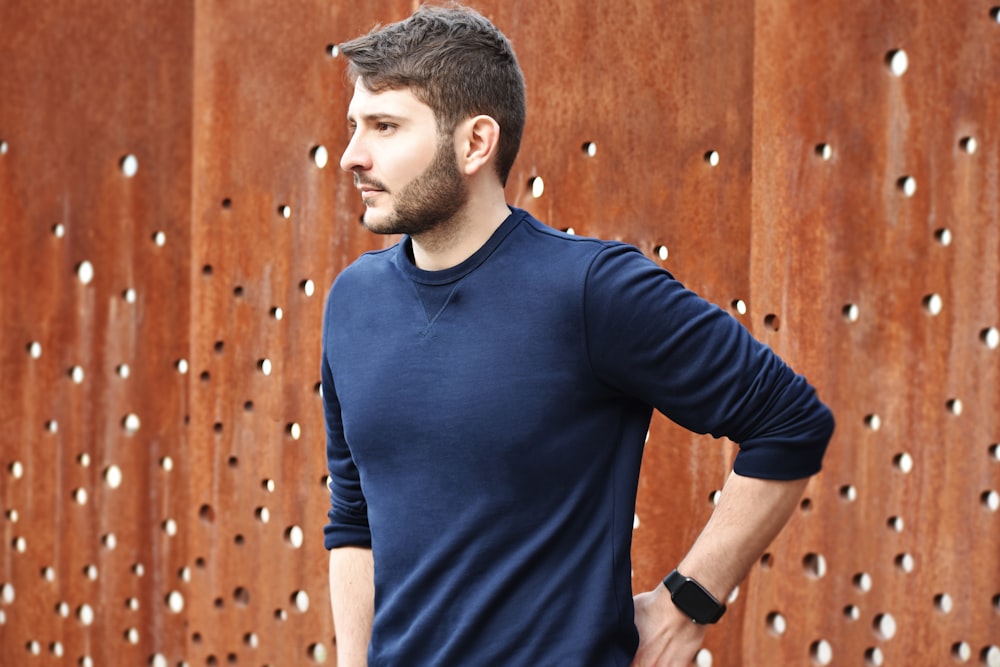 茶色の木製の壁のそばに立つ青いクルーネックTシャツの男