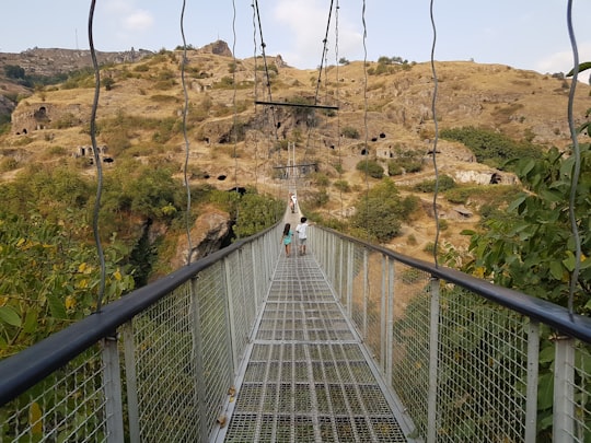 person in white shirt walking on hanging bridge during daytime in Khndzoresk Armenia