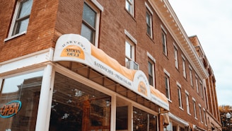 A brick building with multiple windows houses a deli named 'Harvest Moon Deli'. The entrance has an awning with signage advertising sandwiches and fresh salads. There is an 'OPEN' sign visible in one of the windows.