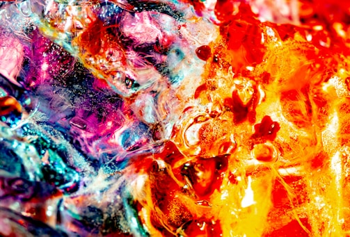 An abstract composition featuring vibrant colors and intricate textures. The swirling patterns create a sense of movement with bold reds, oranges, and blues blending together, resembling a fiery explosion.