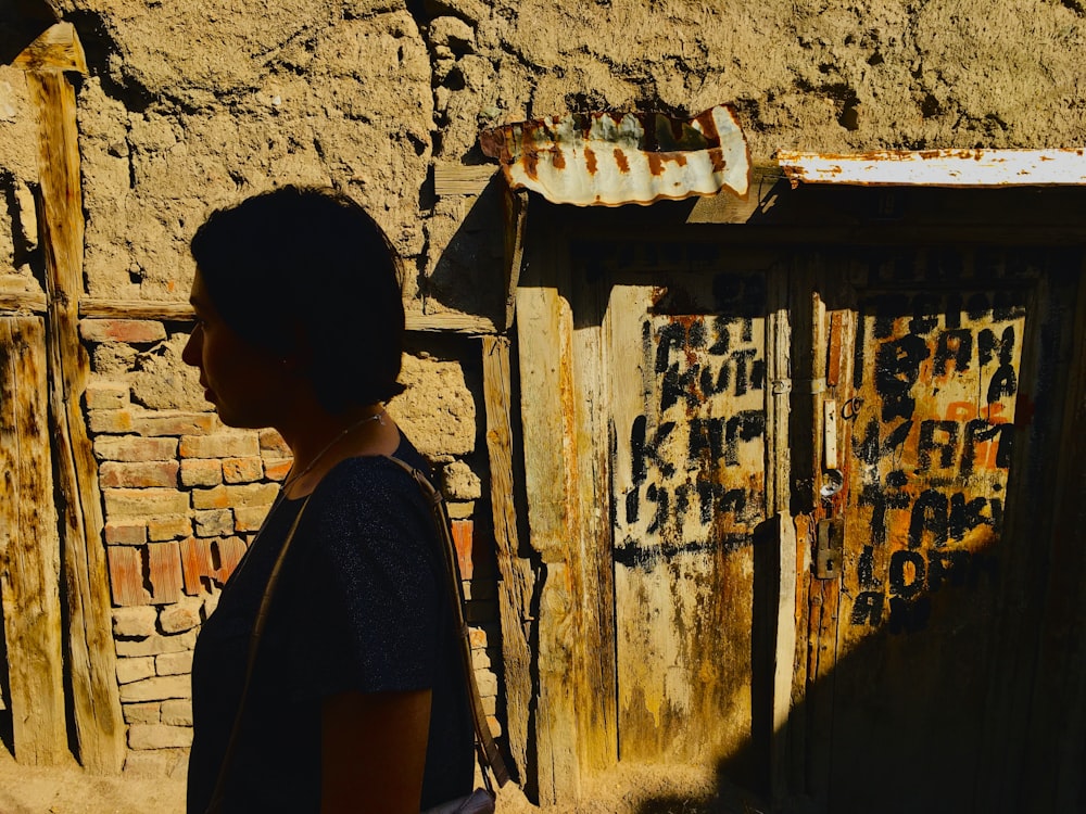 Mujer con camisa negra de pie frente a una pared de concreto marrón