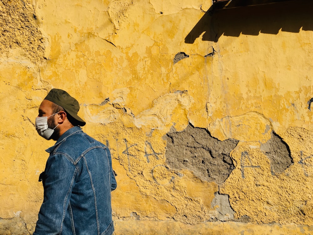 uomo in giacca di jeans blu e berretto nero in piedi accanto al muro marrone