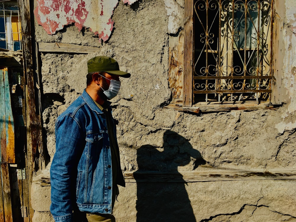 man in blue denim jacket standing near brown wall during daytime