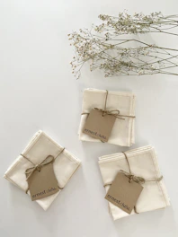 A stack of rustic linen napkins with simple, earthy-toned monograms, styled on a wooden farmhouse table.